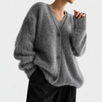 Woman wearing a fluffy, oversized gray cardigan with a V-neck, dark buttons, and long sleeves over black pants.