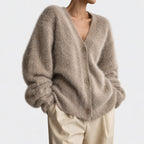 Woman wearing an oversized, fuzzy, light brown cardigan with a V-neck and three visible buttons over beige pants.