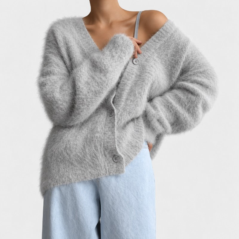 Woman wearing a fuzzy, light gray cardigan with an oversized fit, open neckline, and light blue buttons over light wash jeans.