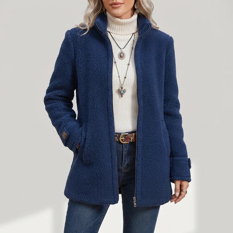 Woman wearing a dark blue sherpa-textured coat with a full zipper, stand-up collar, and side pockets over a white turtleneck.