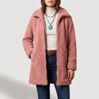 Woman wearing a pink fuzzy coat with a zipper closure, over a cream turtleneck, jeans, and a braided belt.