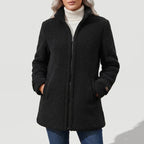 Woman wearing a black full-zip fleece coat over a cream turtleneck, hands in pockets, against a white background.