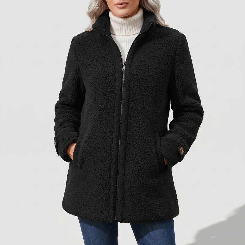 Woman wearing a black full-zip fleece coat over a cream turtleneck, hands in pockets, against a white background.