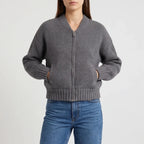 Woman wearing a dark gray ribbed knit cardigan with a silver zipper and front pockets, hands inside.
