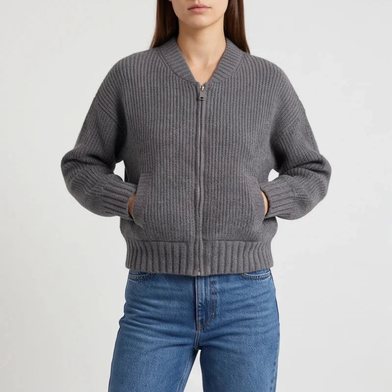 Woman wearing a dark gray ribbed knit cardigan with a silver zipper and front pockets, hands inside.