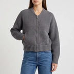 Woman wearing a dark gray ribbed knit zip-up cardigan with front pockets, paired with blue jeans, on a white background.