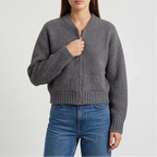Woman zipping up a dark gray ribbed knit cardigan with a silver zipper, worn over blue jeans.