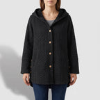 Woman wearing a black quilted hooded jacket with wooden buttons over a gray shirt and blue jeans.