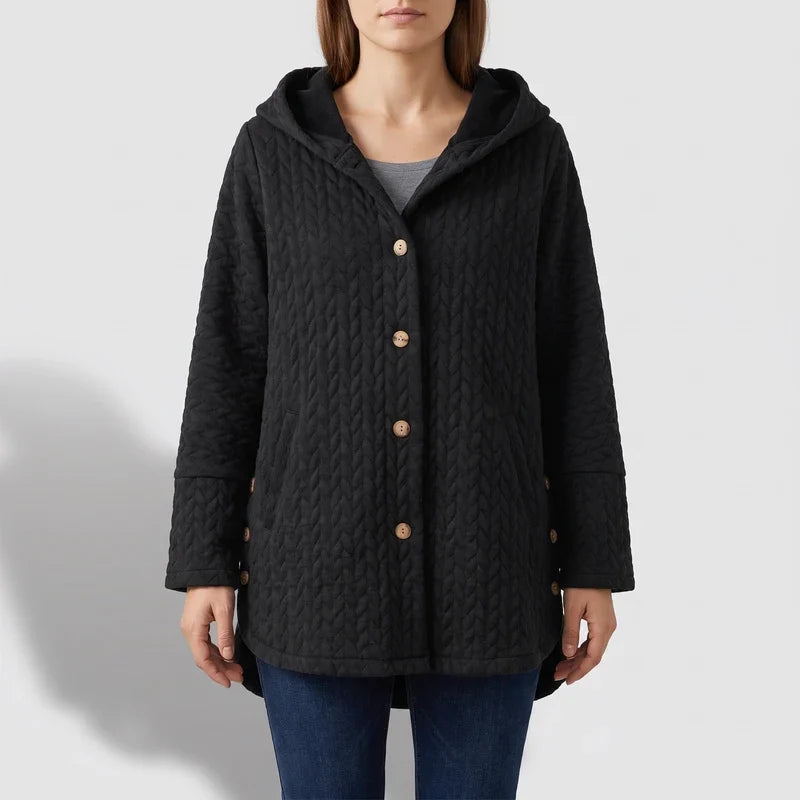 Woman wearing a black quilted hooded jacket with wooden buttons over a gray shirt and blue jeans.