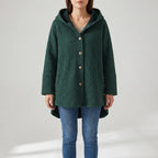 Woman wearing a dark green quilted hooded jacket with wooden buttons and a high-low hem, paired with jeans.
