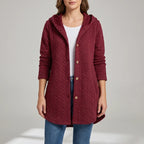 Woman wearing a long-sleeved, deep red quilted hooded jacket with wooden buttons over a white shirt and blue jeans.