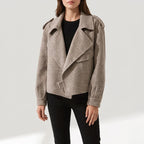 Woman wearing a light brown textured moto jacket with wide lapels, shoulder tabs, and a front buckle.
