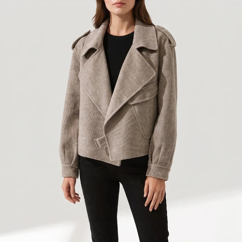 Woman wearing a light brown textured moto jacket with wide lapels, shoulder tabs, and a front buckle.