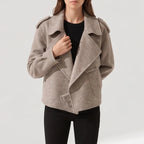 Woman wearing a light beige textured moto-style jacket with wide lapels, shoulder epaulets, and a buckle detail on a white background.