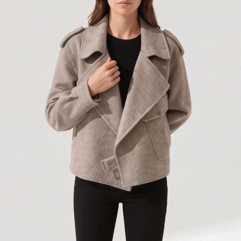 Woman wearing a light beige textured moto-style jacket with wide lapels, shoulder epaulets, and a buckle detail on a white background.