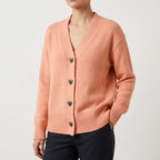 Woman wearing a salmon knit v-neck cardigan with dark antique heart-shaped buttons, ribbed cuffs, and hem.