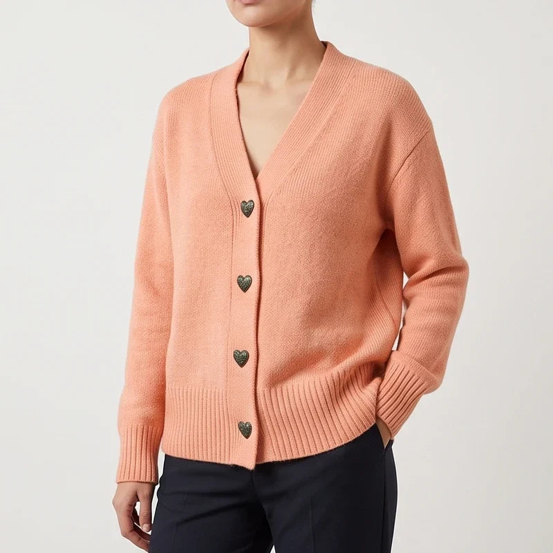 Woman wearing a salmon knit v-neck cardigan with dark antique heart-shaped buttons, ribbed cuffs, and hem.