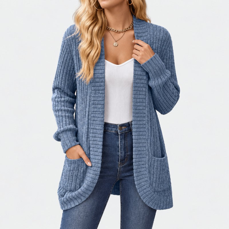Woman wearing a long, blue ribbed knit cardigan with two large front pockets, over a white top and blue jeans.