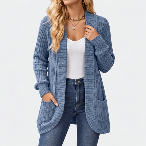 Woman wearing a long, blue ribbed knit cardigan with two large front pockets, over a white top and blue jeans.