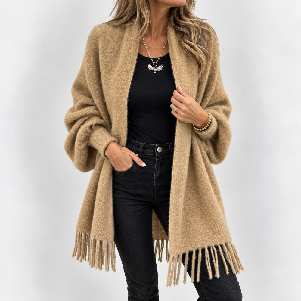 Woman wearing a long, fluffy camel knit cardigan with wide sleeves, fringe detail, over a black top and jeans.