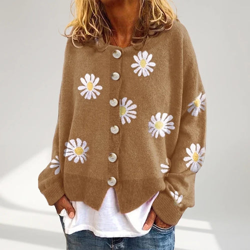 Woman wearing a brown knit cardigan with white and yellow daisy embroidery, buttoned down the front, over a white top.