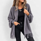 Woman wearing a cozy, open gray knit cardigan with a fuzzy texture and fringed edges, paired with black jeans.