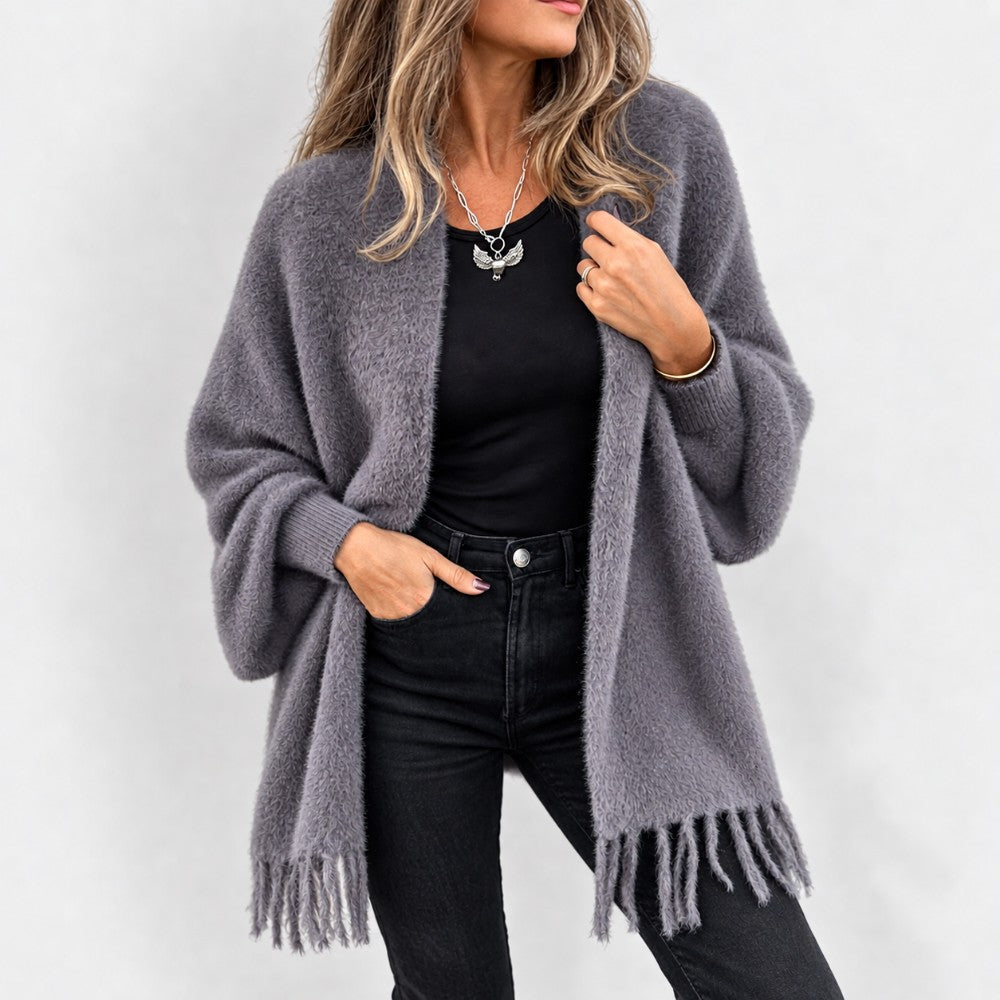 Woman wearing a cozy, open gray knit cardigan with a fuzzy texture and fringed edges, paired with black jeans.