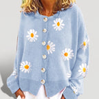 Woman wearing a light blue knit cardigan with white and orange daisy patterns and a front row of white buttons.