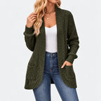 Woman wearing an open dark olive ribbed knit cardigan with two front pockets, over a white tank top and blue jeans.