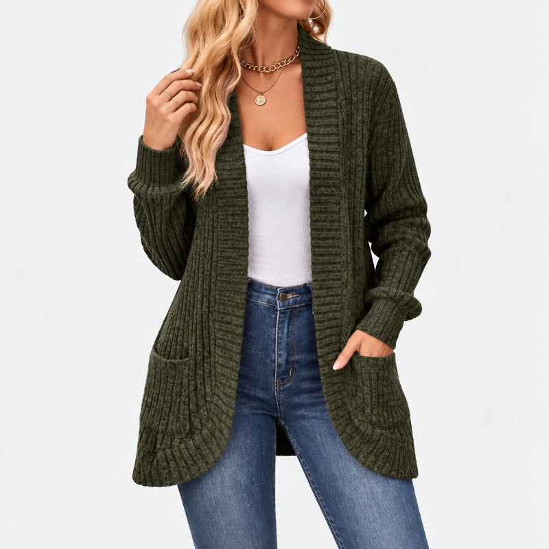 Woman wearing an open dark olive ribbed knit cardigan with two front pockets, over a white tank top and blue jeans.