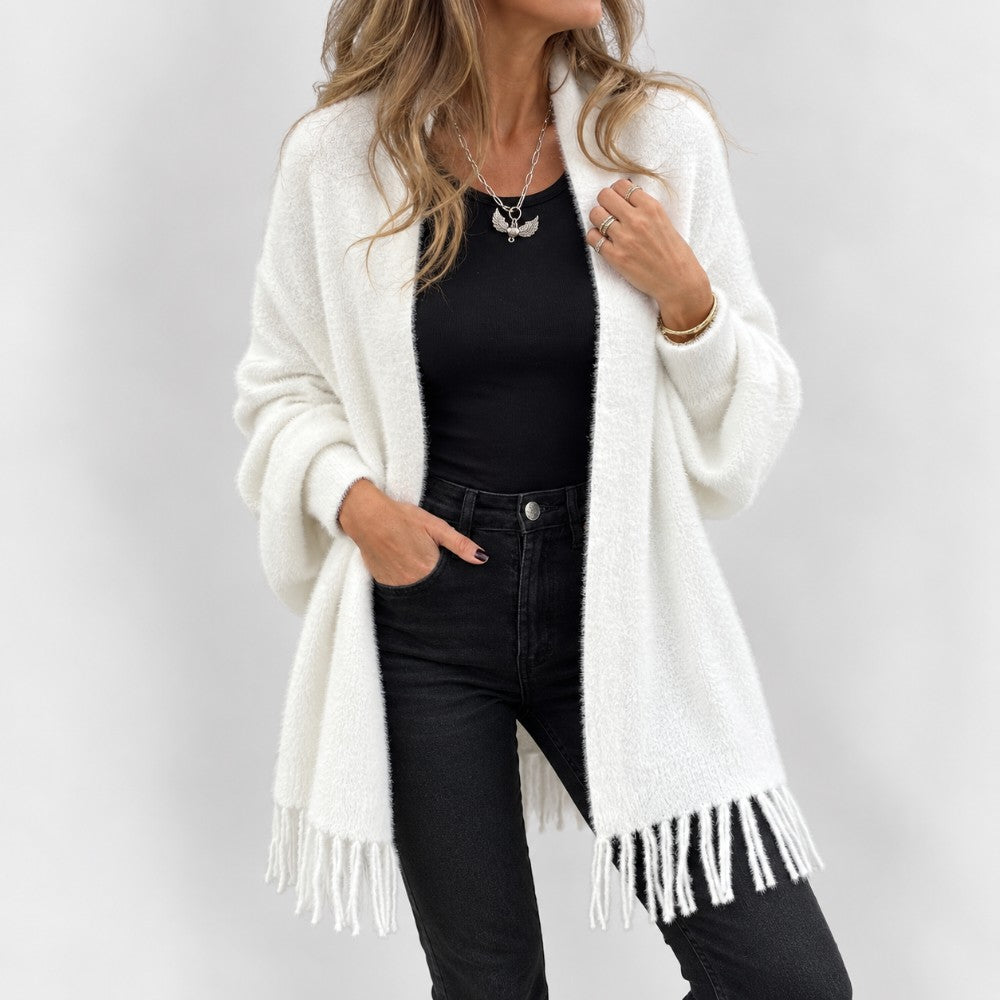 Woman wearing a soft, fuzzy white knit cardigan with fringe edges, paired with a black top and dark jeans.
