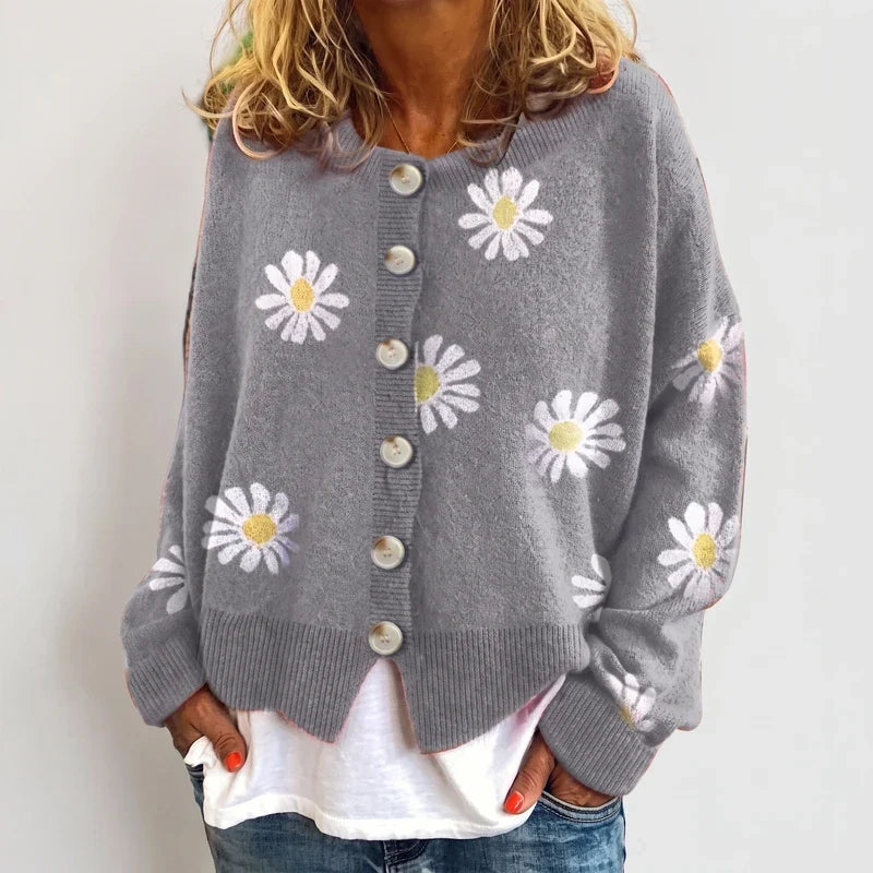 Woman wearing a gray knit cardigan with a white daisy pattern, large button closure, and ribbed hem, over a white top.