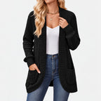 Woman wearing a black ribbed knit open-front cardigan with large pockets, over a white top and blue jeans.