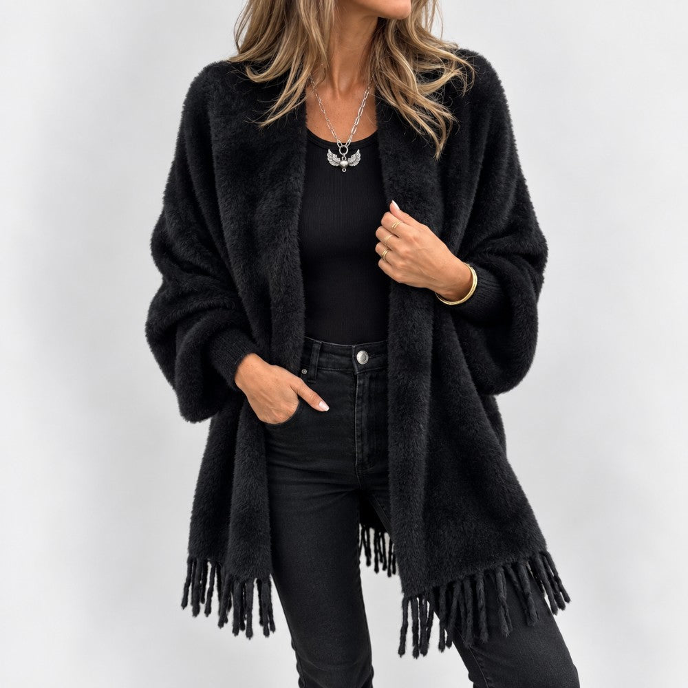 Woman wearing a fluffy black open knit cardigan with fringe, paired with a ribbed black top and black jeans.