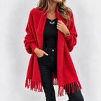 Woman wearing a long, fuzzy red knit cardigan with fringe, over a black top and black jeans.