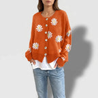 Woman wearing an orange knit cardigan with white and yellow daisy embroidered patterns and light beige buttons.