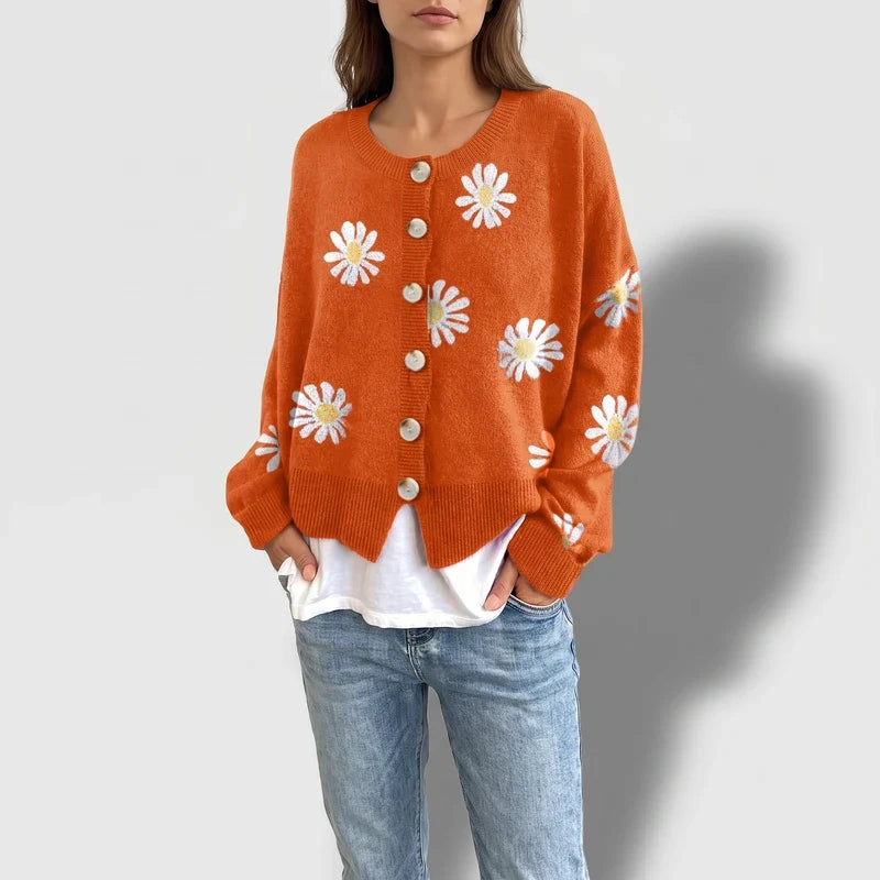 Woman wearing an orange knit cardigan with white and yellow daisy embroidered patterns and light beige buttons.