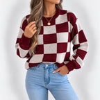 Woman wearing a relaxed-fit, burgundy and cream checkered knit sweater with light wash jeans.