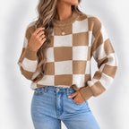 Woman wearing an oversized brown and cream checkered knit sweater with ribbed cuffs and light wash jeans.