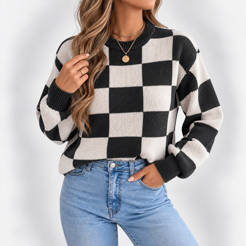 Woman wearing a black and off-white checkerboard knit sweater with blue jeans, a gold necklace, and a ring.