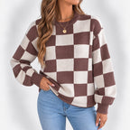 Woman wearing a brown and cream checkerboard knit sweater with ribbed cuffs and a gold pendant necklace.