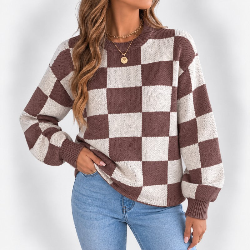 Woman wearing a brown and cream checkerboard knit sweater with ribbed cuffs and a gold pendant necklace.
