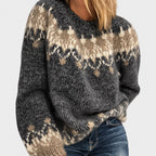 Woman wearing a chunky knit gray, beige, and off-white patterned crewneck sweater with blue jeans.