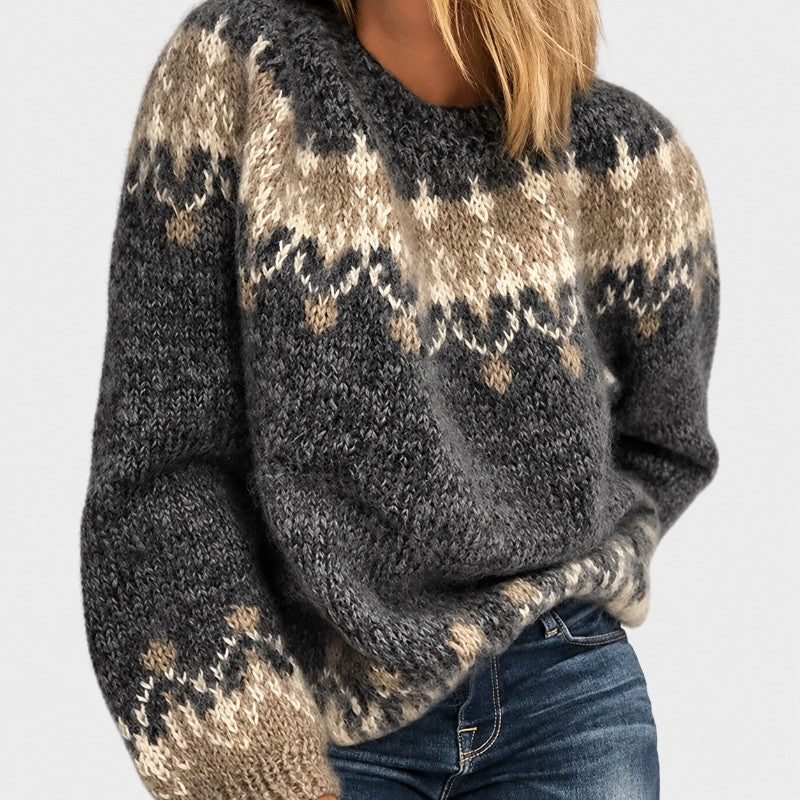 Woman wearing a chunky knit gray, beige, and off-white patterned crewneck sweater with blue jeans.