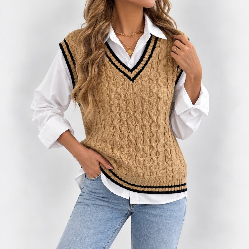 Woman wearing a beige cable knit sweater vest with black and white striped trim over a white collared shirt and blue jeans.
