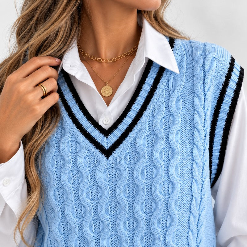 Close-up of a woman wearing a light blue cable knit sweater vest over a white collared shirt with layered gold necklaces.