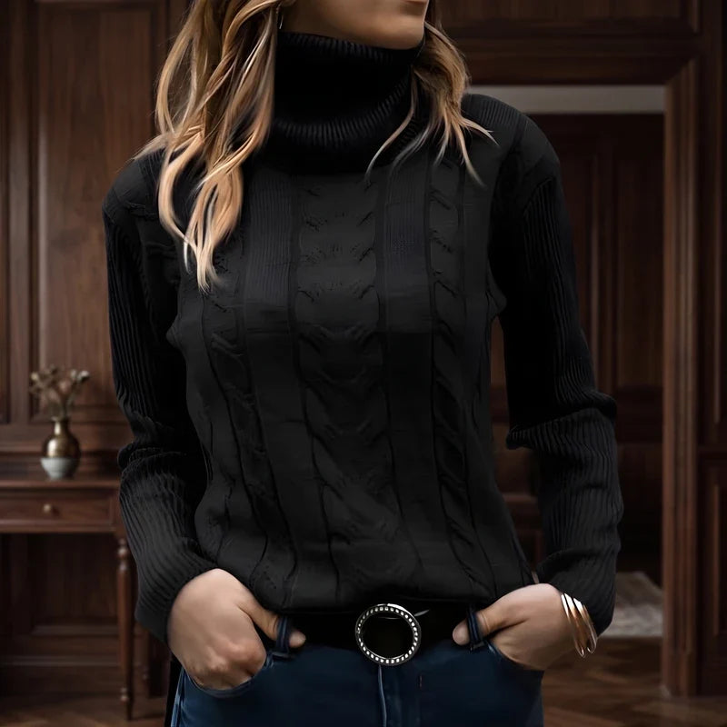 Woman wearing a black cable knit turtleneck sweater with ribbed cuffs and collar, hands in jeans pockets, in a warm wooden room.