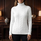 Woman wearing a white cable knit turtleneck sweater with ribbed cuffs and hem, standing in a dim room.