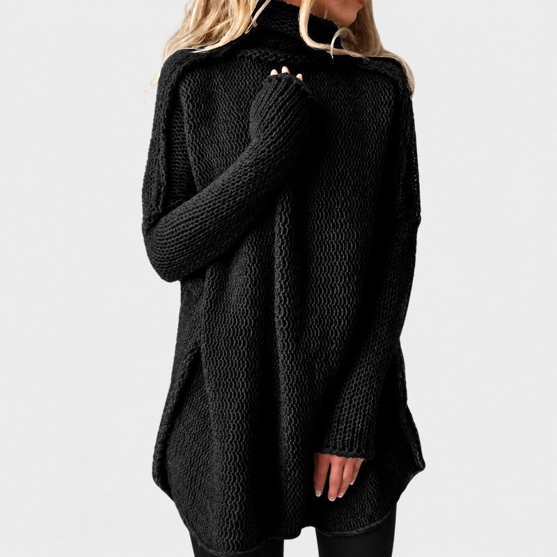 Woman wearing a loose-fitting black knit turtleneck sweater with long sleeves and side slits, against a plain background.