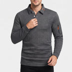 Man wearing a dark grey, waffle-knit long-sleeve polo shirt with two white buttons and an orange zippered sleeve pocket.